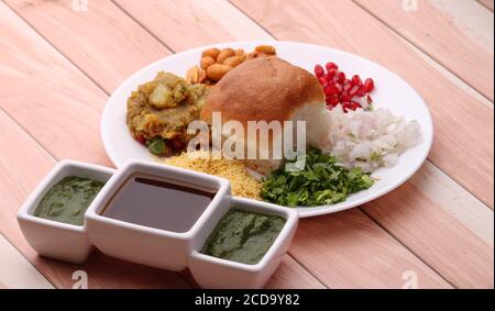 Le Dabeli est un en-cas indien servi avec des graines de grenade et de la coriandre dans une assiette en céramique blanche. Avec chutney vert et chutney de tamarin. Banque D'Images