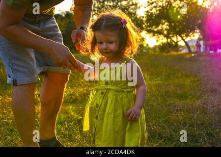 Une petite fille mignonne prend les mains avec son père. Concept de marche avec enfants. Petite fille tenant les mains avec ses parents. Bébé souriant en robe. Banque D'Images