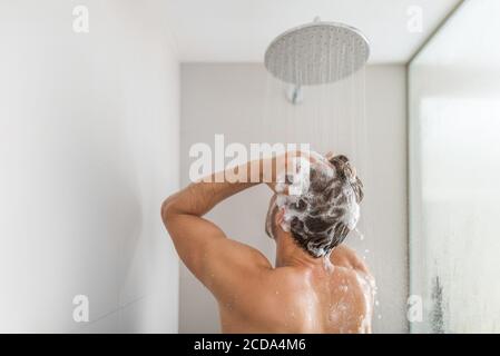 Homme prenant une douche lavant les cheveux sous l'eau tombant de la pomme de douche de pluie dans la salle de bain de luxe. Le style de vie de la jeune personne à la maison. Soins du corps Banque D'Images