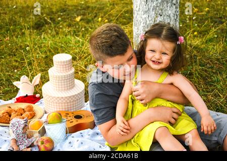 Petit frère jouant avec sa petite sœur. L'embrasser et sourire. Pique-nique d'été en plein air. L'amour de la famille d'abord. Banque D'Images