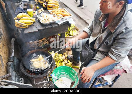 Antananarivo, Madagascar - 24 avril 2019 : une femme malgache locale friture des bananes dans l'huile dans sa stalle sur le marché à côté de la route principale. Plats frais préparés Banque D'Images