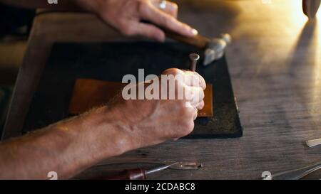 Processus de travail de l'article en cuir dans l'atelier. Homme tenant un outil de fabrication et travaillant dans un foyer doux. Artisan en tannerie. Banque D'Images