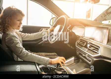 adorable jeune fille caucasienne d'enfant veulent des parents d'acheter cette voiture, elle s'assoit au volant de la nouvelle auto, fille aime lui. dans la concession Banque D'Images