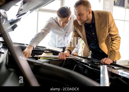 le jeune vendeur de voitures caucasiennes montre la meilleure variante pour le client dans la concession. le beau homme d'affaires est venu pour obtenir une nouvelle auto. le conseiller l'aide avec ch Banque D'Images