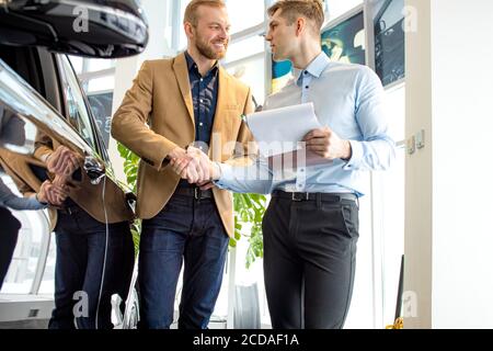 achat réussi à la concession. jeune homme d'affaires achète une nouvelle voiture, il va la main au conseiller. heureux propriétaire de la voiture Banque D'Images