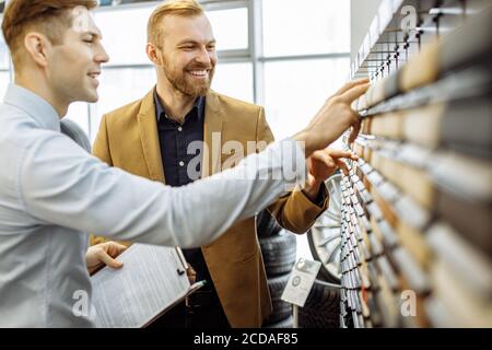 les jeunes clients et les conseillers du caucase regardent la palette de couleurs, choisissent la couleur de la conception de voiture dans la concession Banque D'Images