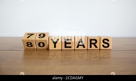 A tourné les cubes et a changé l'expression '79 ans' en '80 ans' ou vice versa. Belle table en bois, fond blanc. Concept d'entreprise, espace de copie Banque D'Images