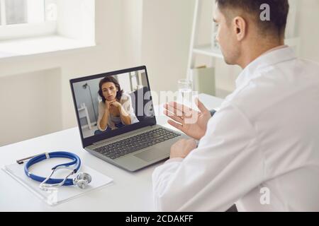 Le médecin donne une consultation en ligne de son bureau médical. Le médecin de sexe masculin utilise un ordinateur portable et écoute son patient. Banque D'Images