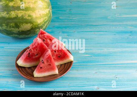 Quatre tranches de pastèque fraîche mûre sont dans une assiette en argile sur une table en bois bleu. Theres un melon d'eau entier dans le fond. Copier l'espace Banque D'Images