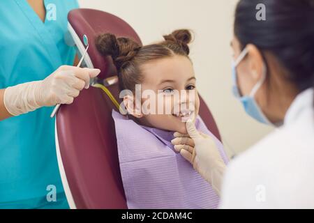 Femme dentiste et assistante examinant les dents souriantes de petite fille dedans clinique dentaire Banque D'Images