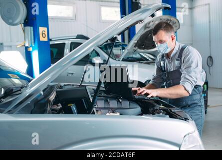 Mécanicien en uniforme et masque de protection travail dans un atelier de voiture. Banque D'Images