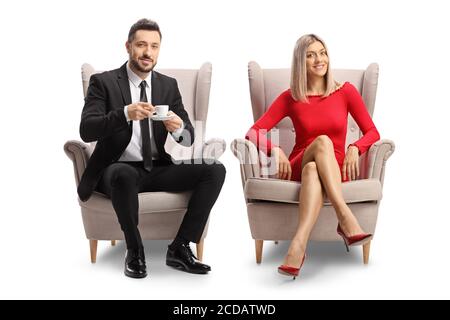Jeune femme blonde vêtue d'une robe rouge et d'un homme avec une tasse de café assis dans des fauteuils isolés arrière-plan blanc Banque D'Images