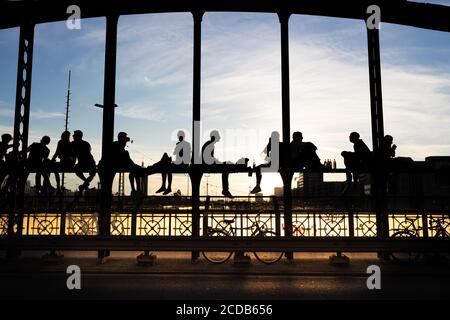 Personnes mal identifiées et rétroéclairées appréciant le coucher du soleil assis sur un pont en acier sur des voies de chemin de fer appelées Hackerbrücke. Munich, Allemagne. Banque D'Images