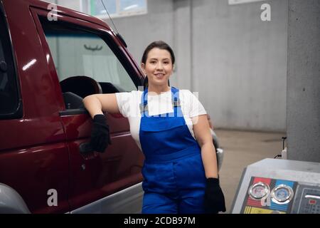 Une femme en uniforme bleu est debout à la voiture et regarde la caméra. Prise de vue moyenne Banque D'Images