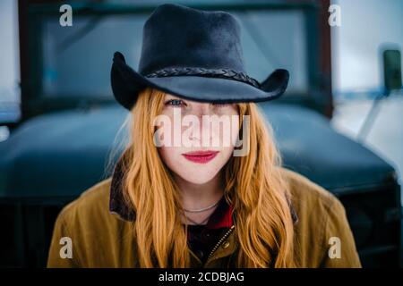 Portrait de belle femme de rancher avec rouge à lèvres rouge et chapeau de cow-boy noir en hiver, yeux bleus, expression confiante Banque D'Images