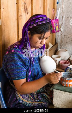 Une jeune femme maya, vêtue d'une robe traditionnelle typique, peint des dessins sur la poterie dans un atelier à San Antonio Palopo, Guatemala. Banque D'Images