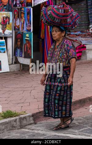 Une ancienne femme maya Tzutujil en costume traditionnel marche dans une rue à Santiago Atitlan, Guatemala, équilibrant son paquet enveloppé dans un tissu de tzute Banque D'Images