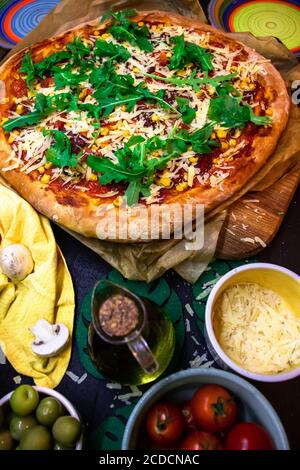 Pizza maison chaude cuite au four avec croûte croustillante servie avec du parmesan et de l'arugula fraîche sur une table de cuisine. Banque D'Images