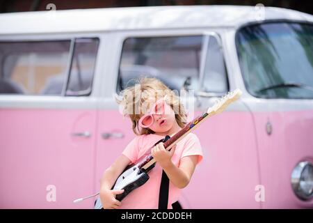 Portrait d'un enfant drôle avec des lunettes roses pratiquant une chanson pendant une leçon de guitare dans la rue. Concept de musique, école de musique pour enfants. Concert de rock. Banque D'Images