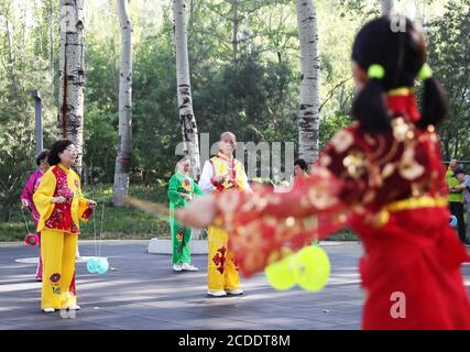 (200828) -- BEIJING, 28 août 2020 (Xinhua) -- Dong Yutong (R) joue du diabolo sous la direction de Dong Shulin (4e L) à la place de la culture Wukesong Diabolo à Beijing, capitale de la Chine, le 11 août 2020. Dong Shulin, 66 ans, vit avec sa femme Mei Yongpei et sa petite-fille de 9 ans Dong Yutong à Beijing. Dong Shulin a commencé à jouer au diabolo en 2003 et maintenant toute la famille aime jouer à ce jeu folklorique traditionnel, dans lequel on peut jeter et attraper un haut tournant en déplaçant un cordon attaché à deux bâtons. Dans la maison de Dong Shulin, plus de 70 diabolos ont été placés tout autour. Certains des diabolos étaient Banque D'Images