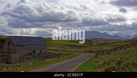 Une Grange en pierre abandonnée avec un toit en ardoise endommagé dans le petit hameau de Balnakiel, avec une petite route sinueuse ou Farm Track. Banque D'Images