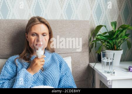 Jeune femme blonde en inhalation avec un nébuliseur à vapeur à la maison. Asthme, grippe, concept de soins de santé. Banque D'Images
