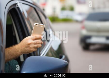 L'homme utilise un téléphone portable depuis une fenêtre de voiture. L'arrière-plan est flou. Copier l'espace. Banque D'Images