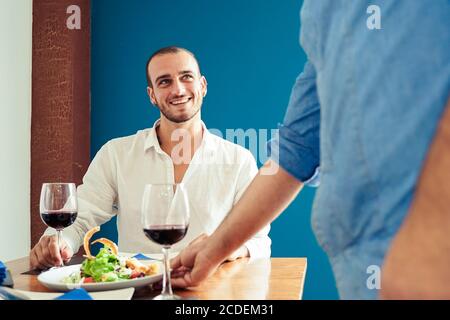 Chef de cuisine présentant la nourriture aux clients dans le restaurant. Les chefs présentent une assiette de poulet à salade avec du riz et des légumes. Joyeux jeune homme en attente Banque D'Images