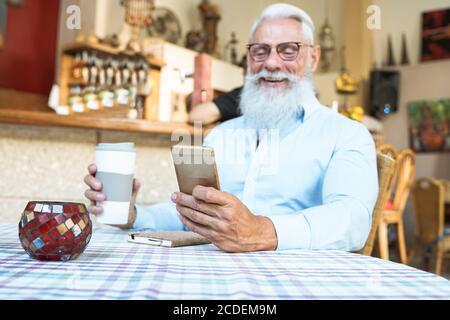 Homme expérimenté heureux utilisant l'application pour smartphone. Vieil homme utilisant une nouvelle technologie tendance. Homme buvant un délicieux café. Concept de mode de vie des personnes âgées. Concentrez-vous sur son ha Banque D'Images