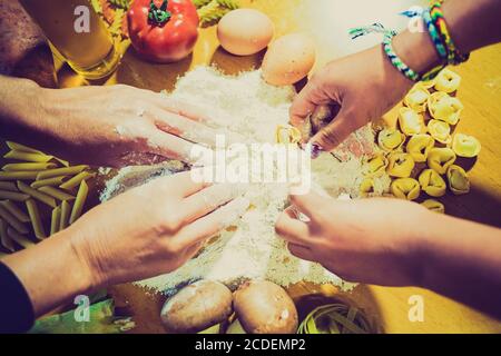Cuisine familiale de pâtes maison, les mains de maman et la fille dans la farine sur un fond de table en bois. Différentes pâtes avec légumes et œufs - image Banque D'Images