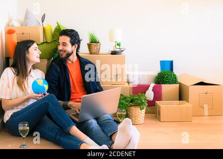 Un jeune couple heureux s'amusant à utiliser un ordinateur portable pour faire des achats en ligne. Newlyweds assis à côté boîte carton dans la nouvelle maison de propriété. Louer, acheter et personnes lif Banque D'Images