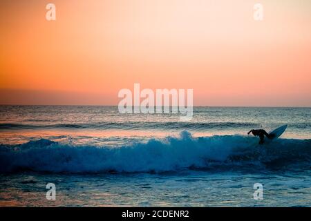 La silhouette d'un surfeur qui fait une vague sur un point de surf vide. Un jeune surfeur passe la vague au coucher du soleil. Image Banque D'Images