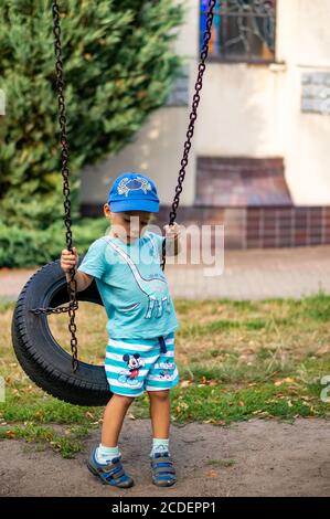 POZNAN, POLOGNE - 24 août 2020 : jeune petit garçon caucasien polonais de trois ans assis sur une balançoire avec des pneus dans une aire de jeux. Banque D'Images