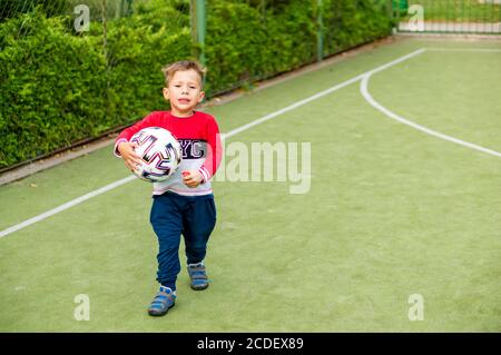 POZNAN, POLOGNE - 20 août 2020 : petit garçon caucasien polonais triste de trois ans tenant un football sur un terrain de football vert. Banque D'Images