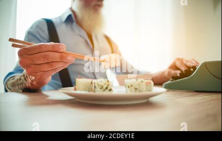 Homme appréciant manger des sushis asiatiques frais et colorés à l'aide de baguettes. Cet homme écrit avec l'ancienne machine à écrire dans le bureau. Image Banque D'Images