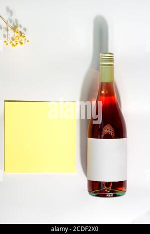 Carte postale de félicitations avec bouteille de vin rose, fleur naturelle tendre et carte postale dans une enveloppe sur fond gris clair avec ombres, copie s. Banque D'Images