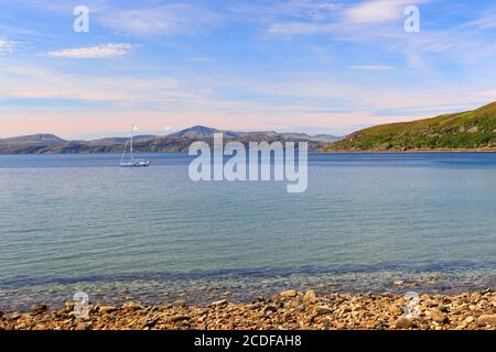 Vue panoramique prise de l'APPLECROSS de mer calme et d'un yacht à voile lors d'une belle journée d'été avec l'île de Rassay en arrière-plan. Highlands écossais Banque D'Images