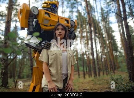 Cosplayer à l'image d'un robot transformateur et fille se tiennent ensemble parmi la forêt. Banque D'Images