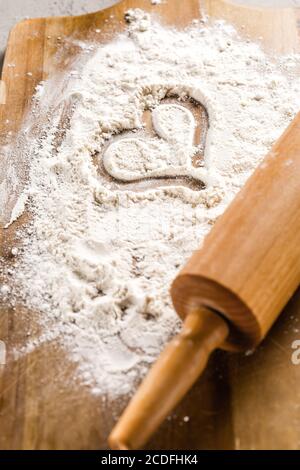 Broche à roulettes en forme de coeur dans la farine sur une planche à découper en bois. J'adore le concept de pâtisserie Banque D'Images