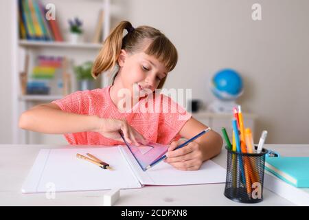 Fille souriante faisant le travail de classe à la maison travaillant avec un règle sur un ordinateur portable sur un bureau Banque D'Images