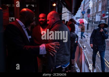 Lors d'une nuit de pluie à Soho, les buveurs masculins se cachent sous une verrière et une lumière rouge chaude à l'extérieur du pub « Nellie Dean of Soho » sur Dean Street, alors que les bars et les restaurants récemment rouverts sont désespérés pour faire affaire pendant la pandémie du coronavirus, le 27 août 2020, À Londres, en Angleterre. Banque D'Images