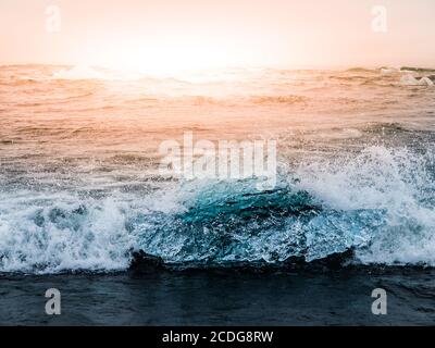 Les icebergs ont été écrasés par les vagues de la mer sur la plage noire au lever du soleil près du lac glacier de Jokulsarlon, en Islande. Banque D'Images