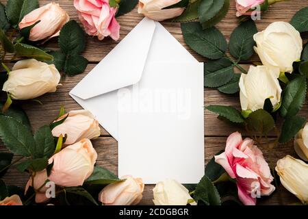 Vue de dessus des enveloppes entourées de roses sur un surface en bois Banque D'Images