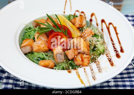 Nouilles de riz au saumon et aux épinards. Déjeuner dans une assiette blanche sur la table. Tomates, citron, poisson, romarin, soi et graines de sésame. La nourriture reste vie Banque D'Images