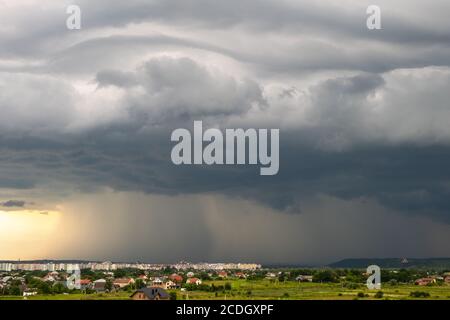 Paysage de Moody avec des nuages sombres de tempête avec chute de pluie de pluie déversante de pluie sur les bâtiments éloignés de ville en été. Banque D'Images