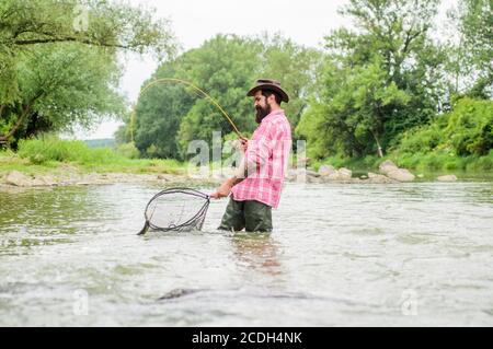 week-end d'été. Pêche au gros gibier. Pêcheur barbu dans l'eau. Activités de loisir et de sport. Pothunter. Homme mature pêche à la mouche. Homme attrapant le poisson. Pêcheur avec canne à pêche. Le vieil homme et la mer. Banque D'Images