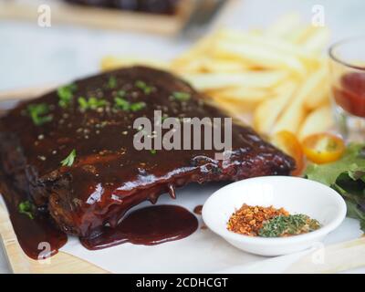 Côtes de porc grillées à la sauce barbecue et caramélisées Miel avec en-cas de frites sur une assiette en bois Banque D'Images