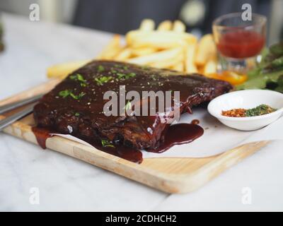 Côtes de porc grillées à la sauce barbecue et caramélisées Miel avec en-cas de frites sur une assiette en bois Banque D'Images