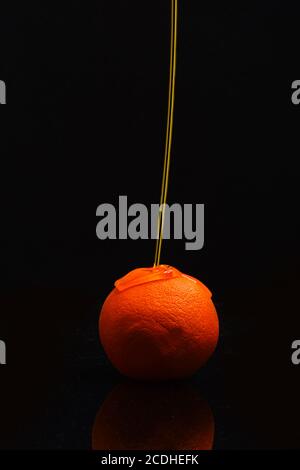 Jus d'orange éclaboussant sur les fruits d'orange. Jus ou miel versés sur des fruits sur fond noir. Orange ou pamplemousse couvert d'ombres. Concept de nutrition et d'art alimentaire Banque D'Images