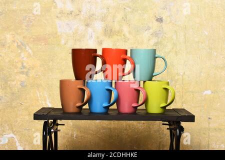 Table basse et tasses lumineuses et élégantes de différentes couleurs. Table avec tasses colorées sur fond de mur. Table basse moderne avec différentes capsules de thé ou de café près du mur. Concept de maison confortable et de batterie de cuisine. Banque D'Images